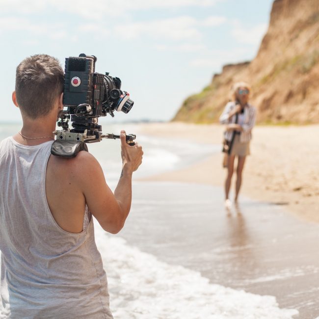 Professional videographer- film maker filming music clip on sand coast - beach near sea.